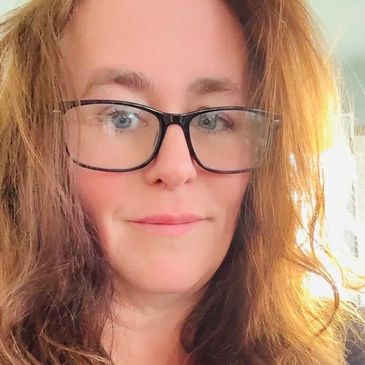 Woman with glasses and wavy hair smiling gently.