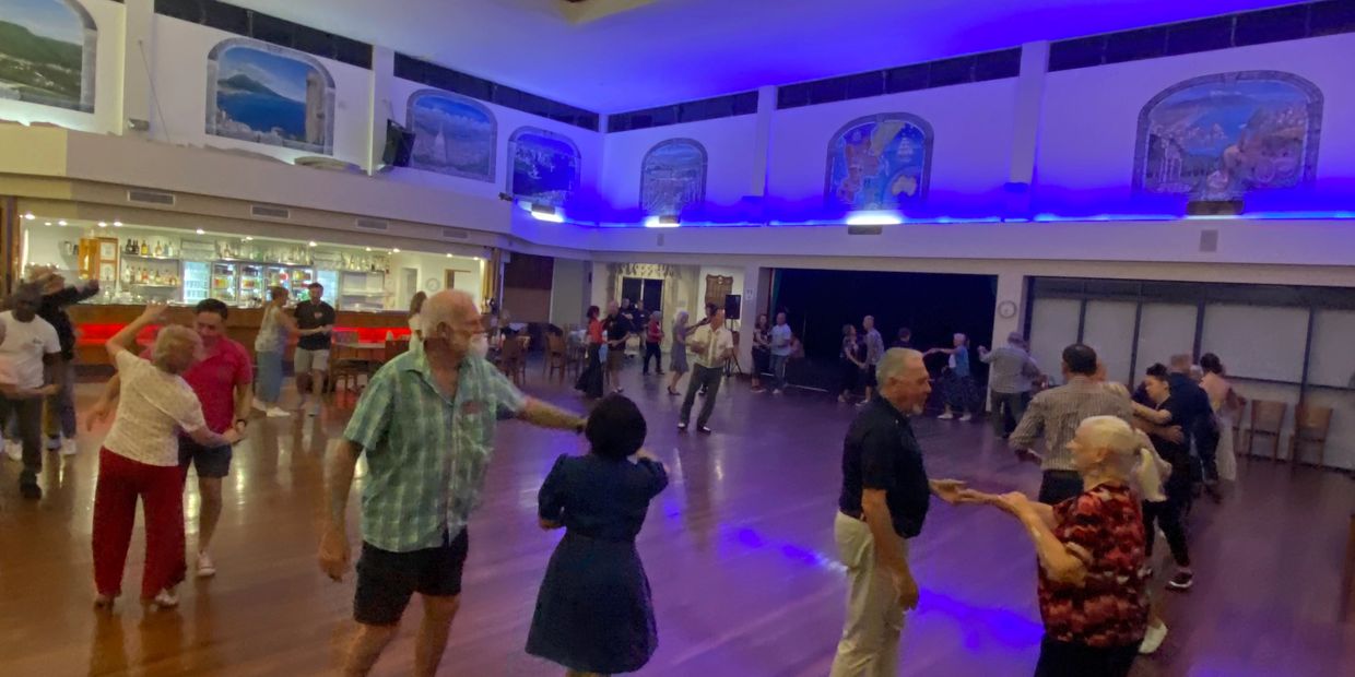 People dancing in a spacious hall with blue ambient lighting.