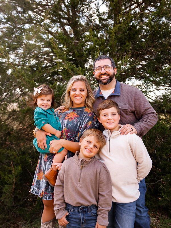 Happy family of five posing outdoors with smiles and warm clothing.