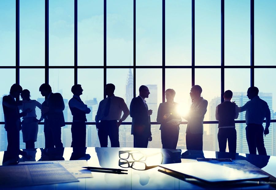 Business professionals conversing in a modern office with city views and sunlight.