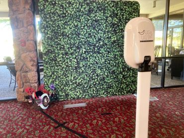 Photo booth setup with greenery backdrop indoors.