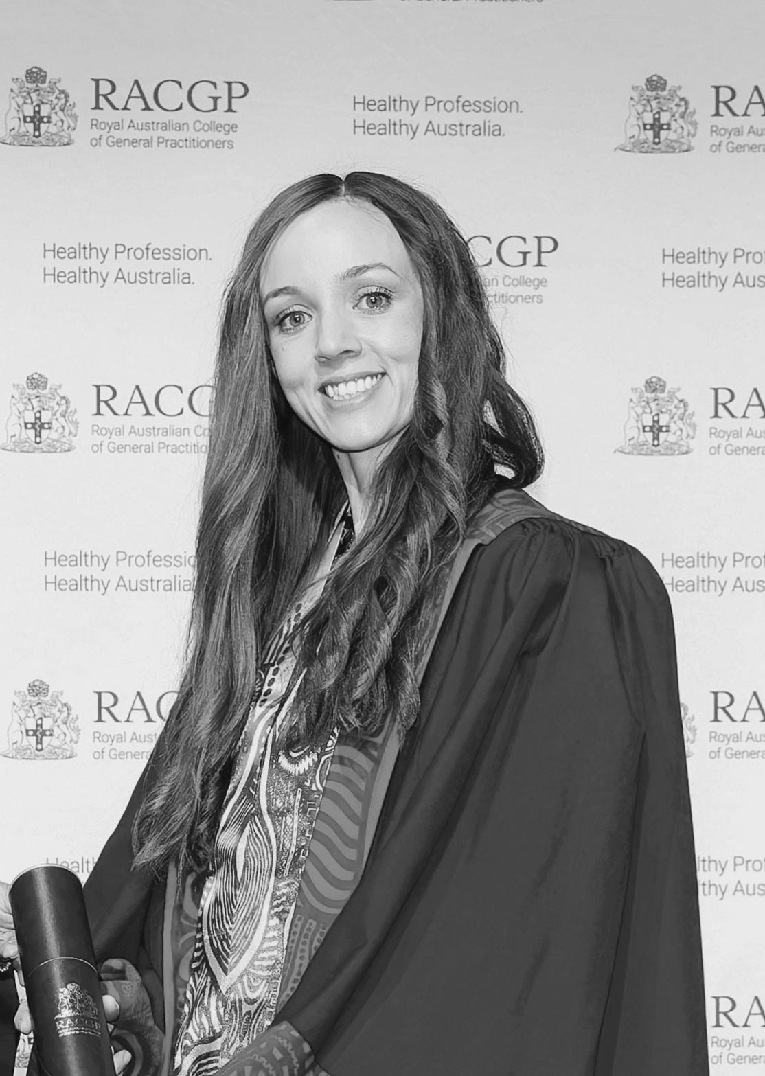 Smiling graduate in blue and red robe holding diploma at RACGP event.
