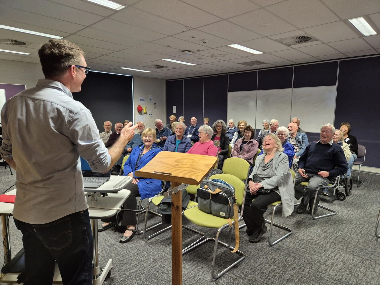 A man is presenting a workshop to a roomful of happy people
