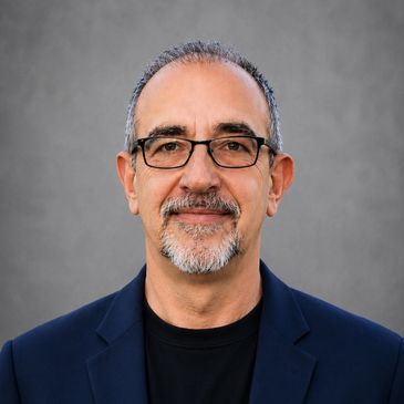 Portrait of a middle-aged man with glasses and a beard, wearing a dark blazer.