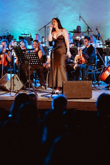 Woman singing on stage with orchestra.