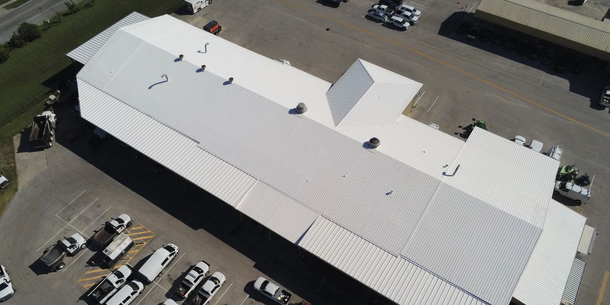 Aerial view of a large white-roofed industrial building with parked vehicles.
