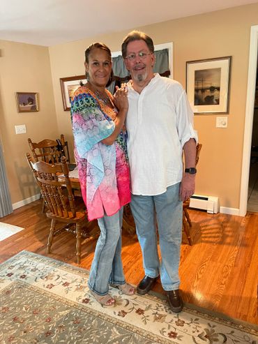 A couple standing and smiling inside a cozy dining room.