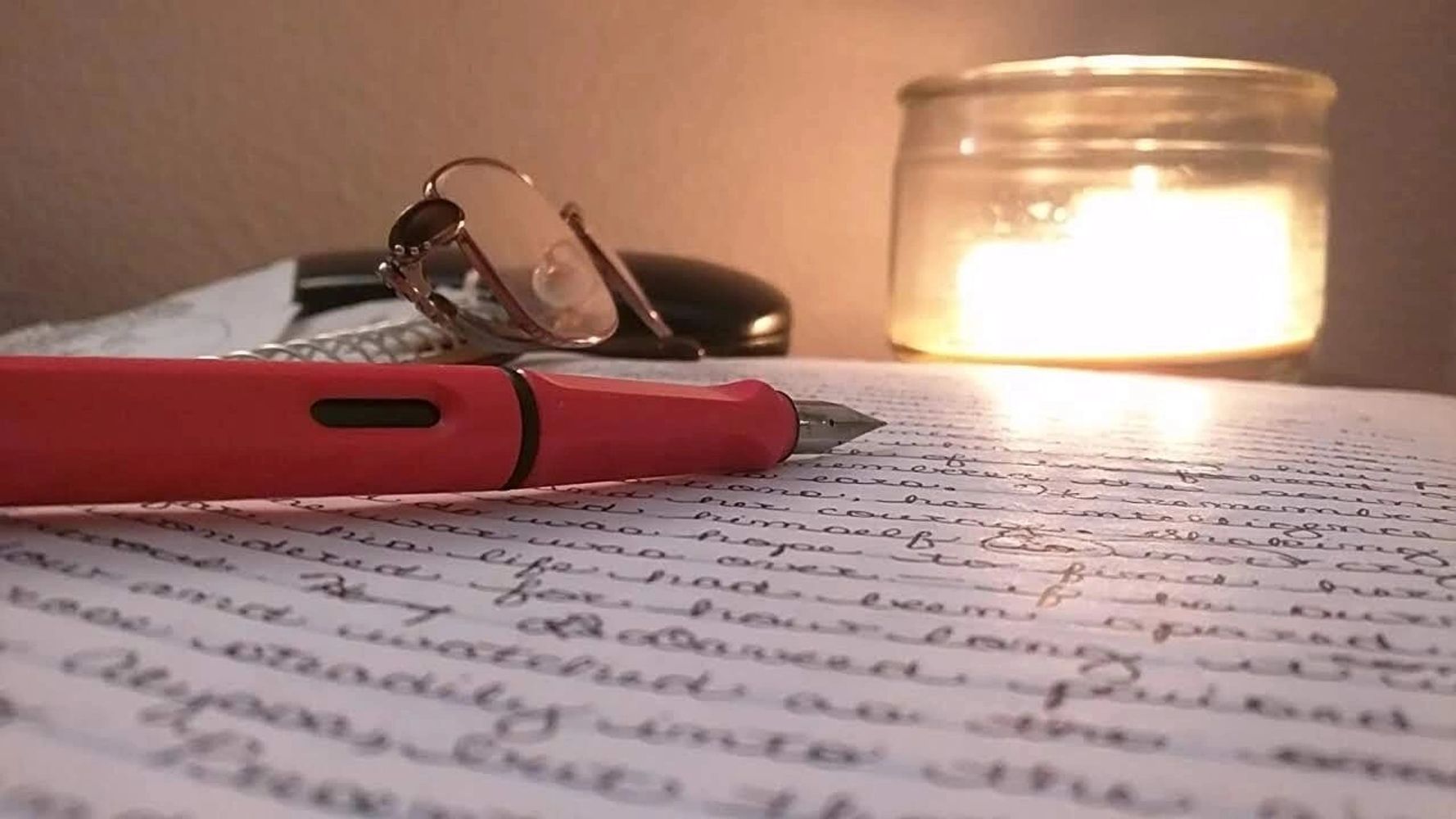 A fountain pen resting on a manuscript, lit by candlelight.
