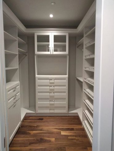 Empty modern walk-in closet with white shelves and wooden floor.