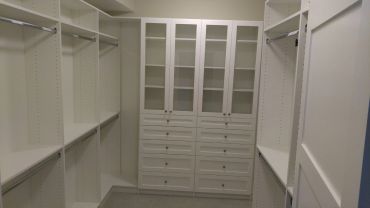 Empty walk-in closet with white shelves and glass-paneled cabinets.