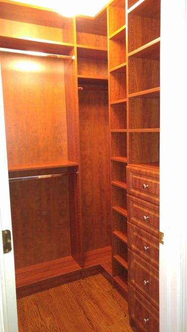 Empty wooden walk-in closet with shelves and drawers.