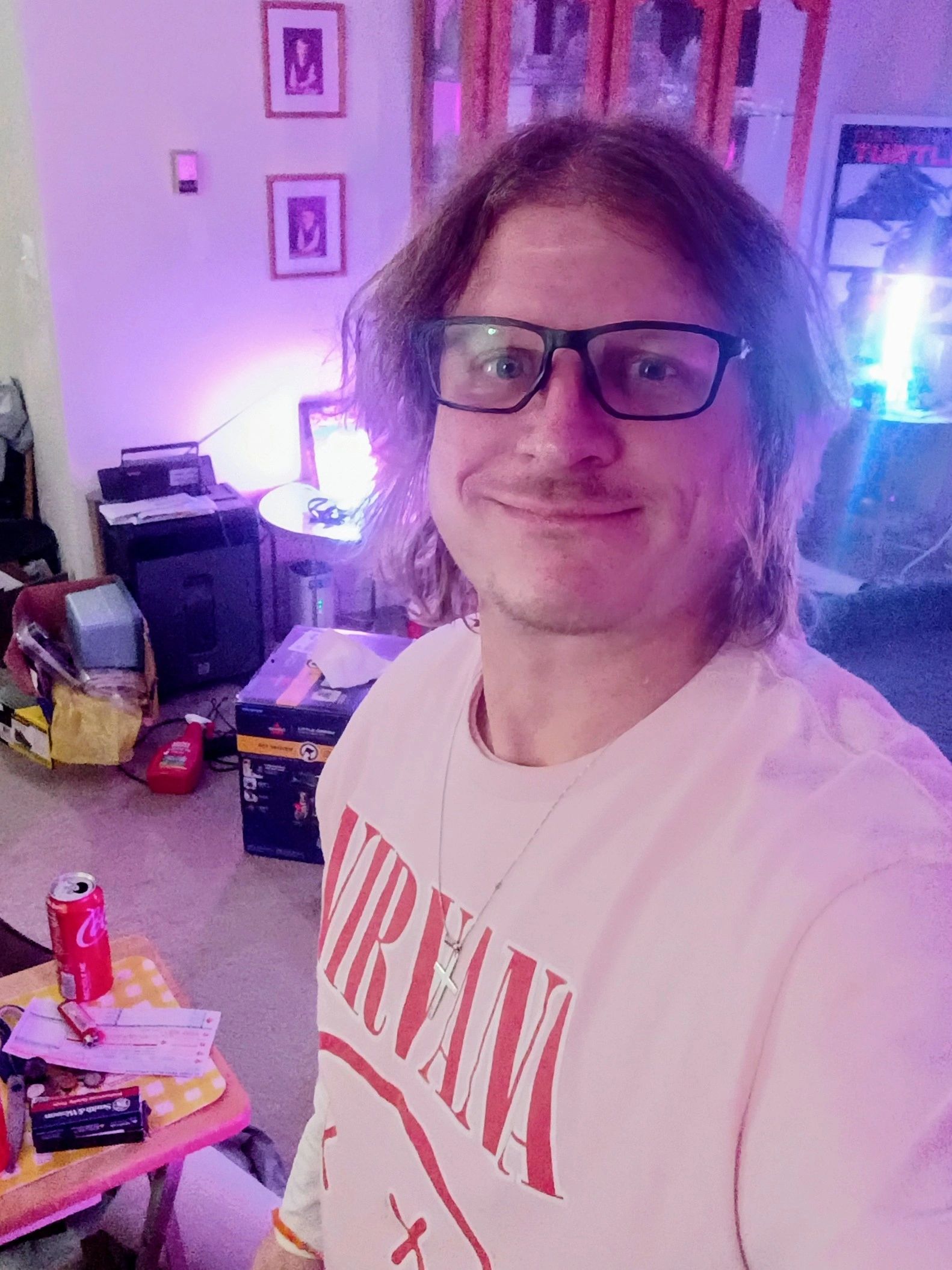 Person smiling in a room with purple lighting and casual clutter.