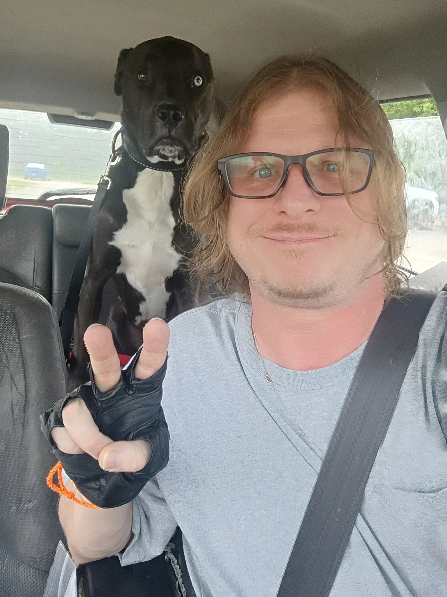 Man with glasses and dog giving a peace sign inside a car.