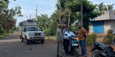 Three men talking on a road with a vehicle and scooters.