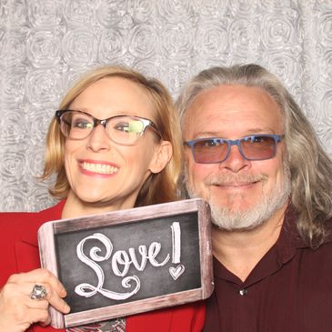 Ivy and Chris smiling and holding up a sign that says love on it. 