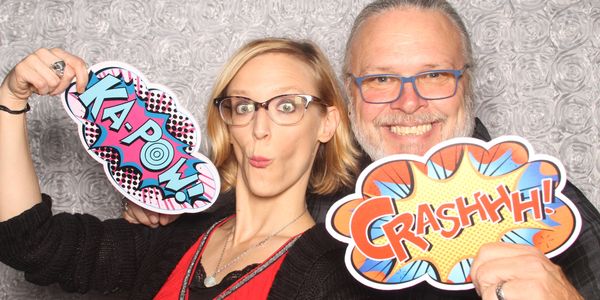 Chris and Ivy posing in Hey Photobooth with a 'Ka-pow!' sign making a silly face and a 'Crashhhh' te