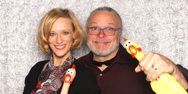 Smiling photo of Ivy and Chris holding the famous rubber chicken props in Hey Photobooth.