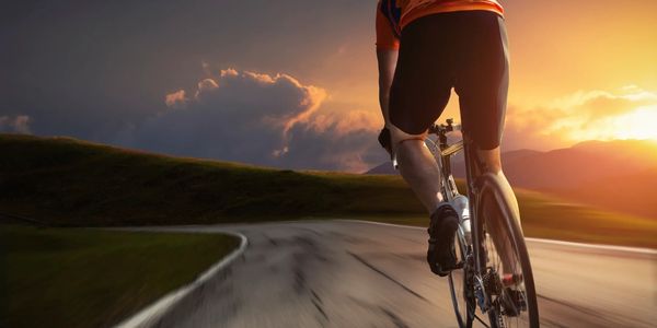 Cyclist riding on blurred road towards hills with sun setting in background