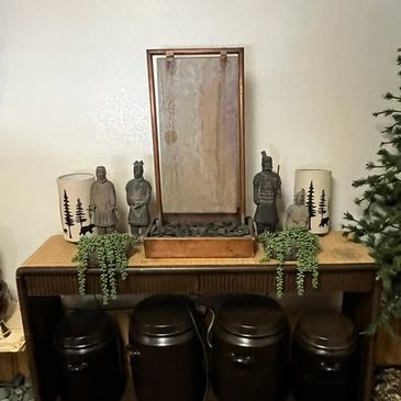 A wooden table with decorative statues, plants, and four dark containers underneath.