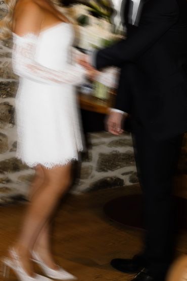 A blurred image of a couple holding hands, the woman in a white dress and the man in a black suit.
