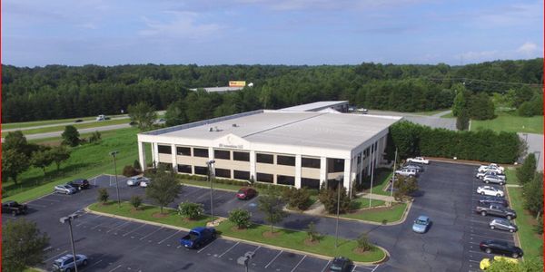 A large office building surrounded by a parking lot and greenery.