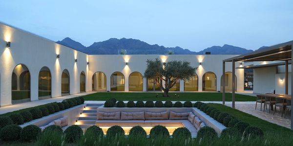 Elegant courtyard with sunken seating, arched windows, and mountain backdrop at dusk.