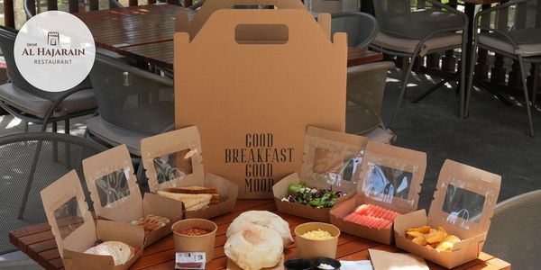 Breakfast spread in eco-friendly packaging on a wooden table at Al Hajarain Restaurant.