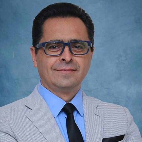 Hombre con gafas y traje claro sonriente.