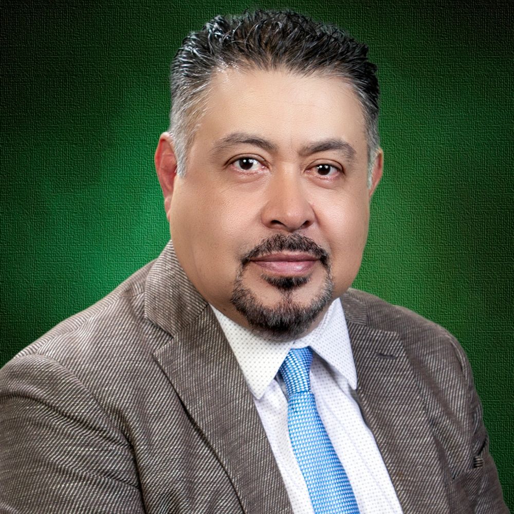 Hombre con traje marrón y corbata azul sobre fondo verde.
