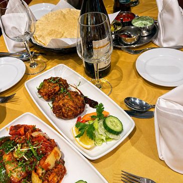 Indian meal with pakoras, curry, and wine on a yellow tablecloth.