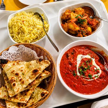 A platter with naan, yellow rice, curry, and a creamy tomato dish.