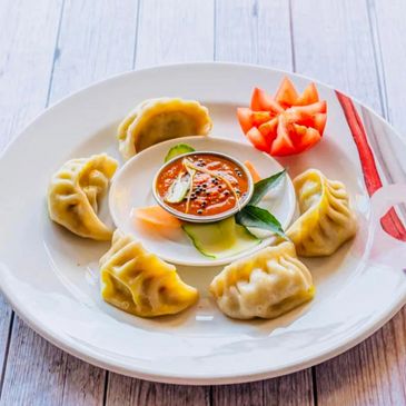 Plate of steamed dumplings with dipping sauce and tomato garnish.