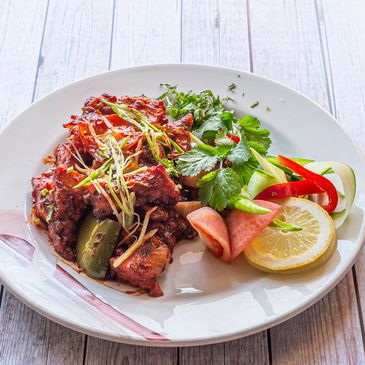 Spicy grilled meat with fresh vegetable garnish and lemon slice on white plate.