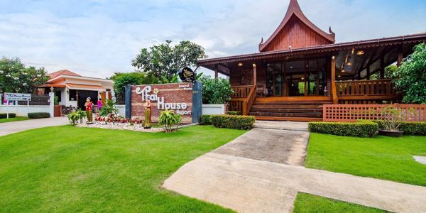Traditional Thai-style wooden resort building with lush green lawn.