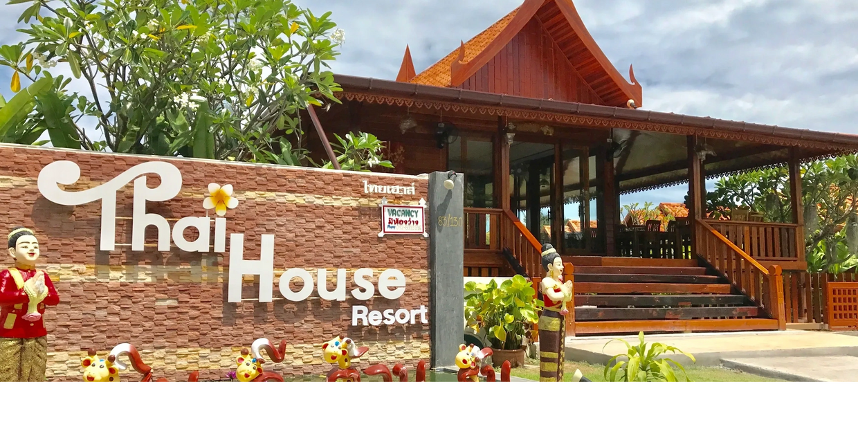 Thai House Resort entrance with traditional wooden architecture and decorative statues.
