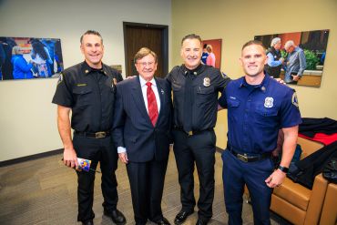 Group of men smiling indoors, two in uniforms.