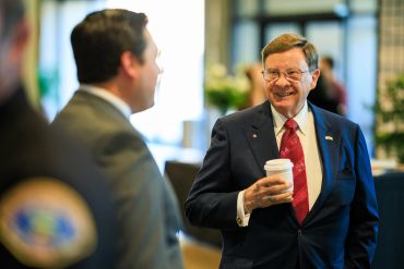 Two men in suits having a conversation, one holding a coffee cup.
