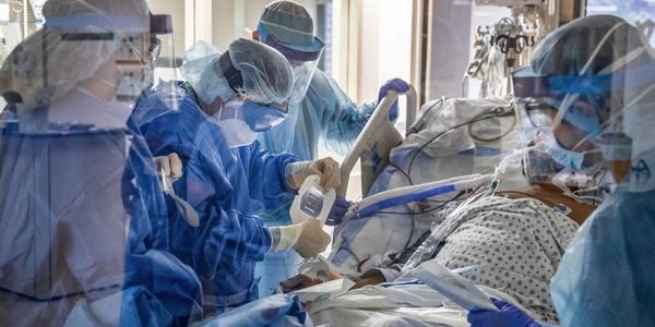 Hospital staff including doctor and nurses attending to one COVID-19 patient in a hospital ward bed.