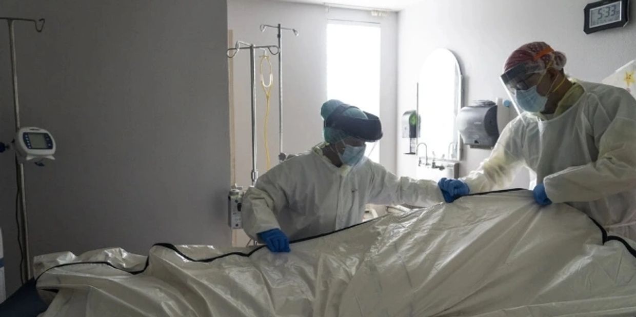 Hospital staff dealing with the aftermath of a patient death within a ward, wearing extensive PPE.