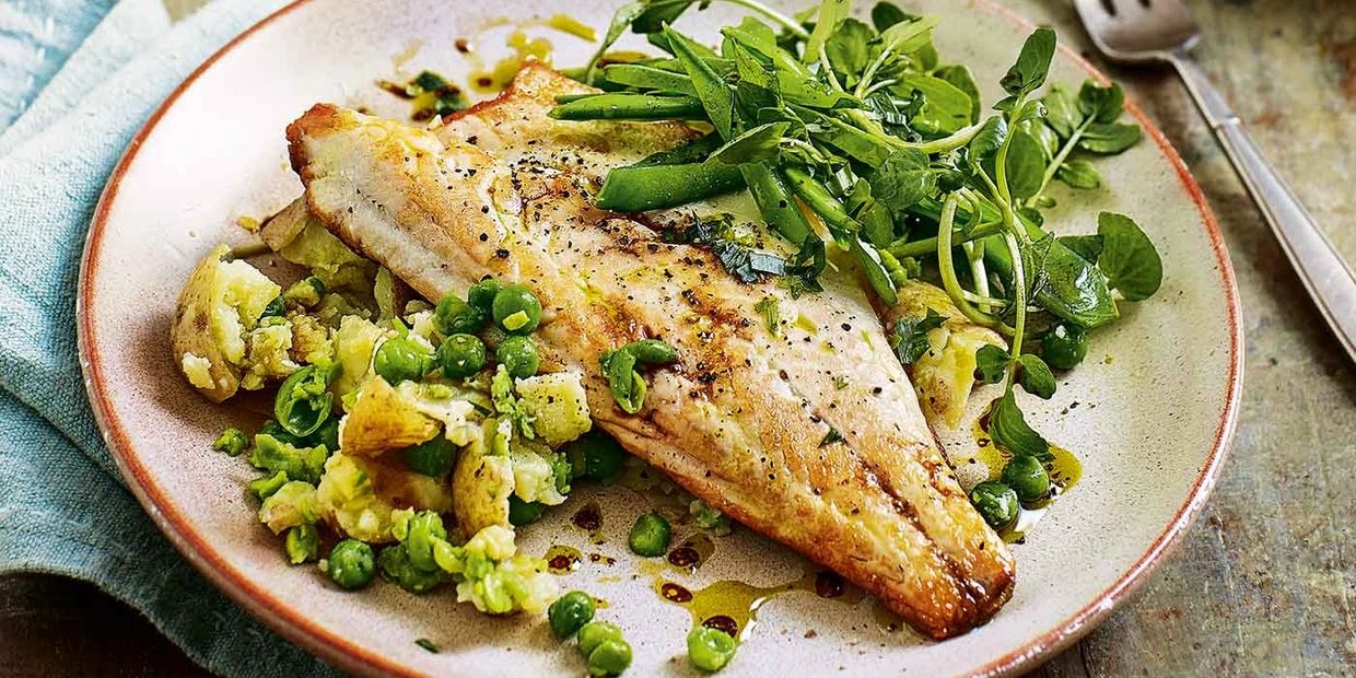 Sea bass with rocket salad. green peas and cauliflower, with a garnish of herbs, on plate with fork.