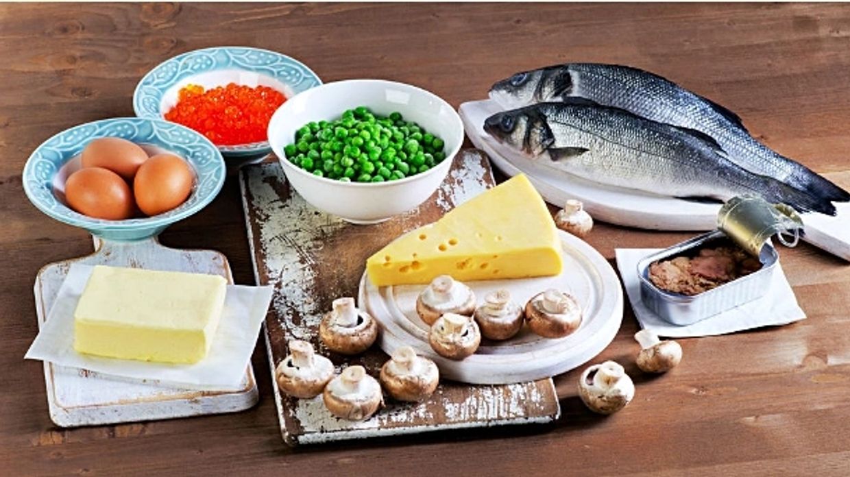 Group of foods with Vitamin D content, including fresh fish, eggs, cheese, peas, mushrooms, butter.