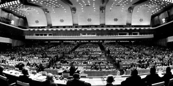 B&W Photograph of auditorium within the WHO building with many countries' representatives attending.