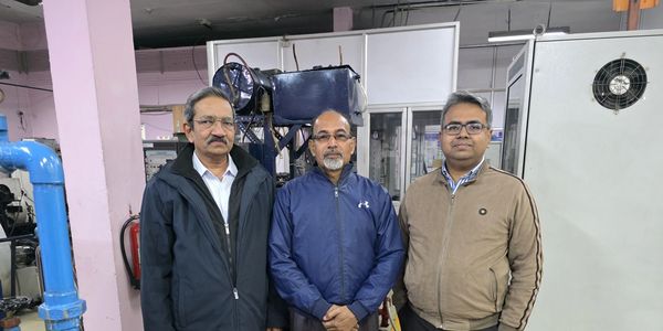 Three men standing in an industrial setting with machinery.