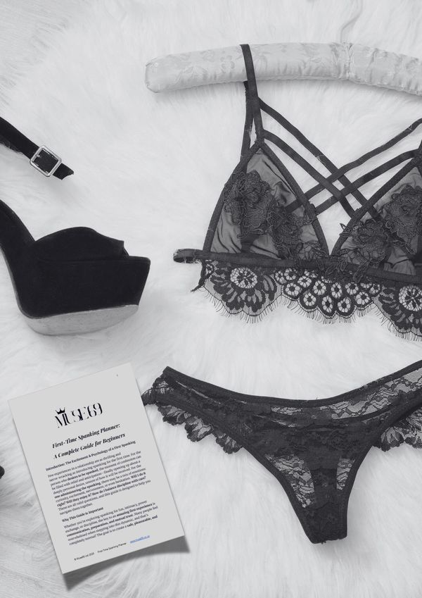 Black lace lingerie set with high heels and a first-time spanking planner on a white fur surface.