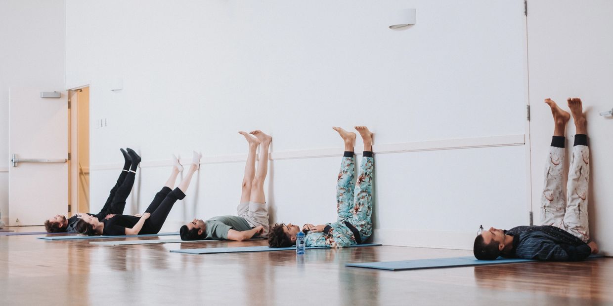 group of people in a movement class layaing on yoga mats and their legs resting on the wall.