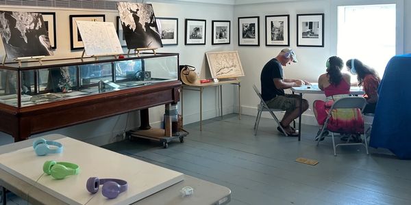 Three people sit at a table beside a window and examine a map in a room full of maps.