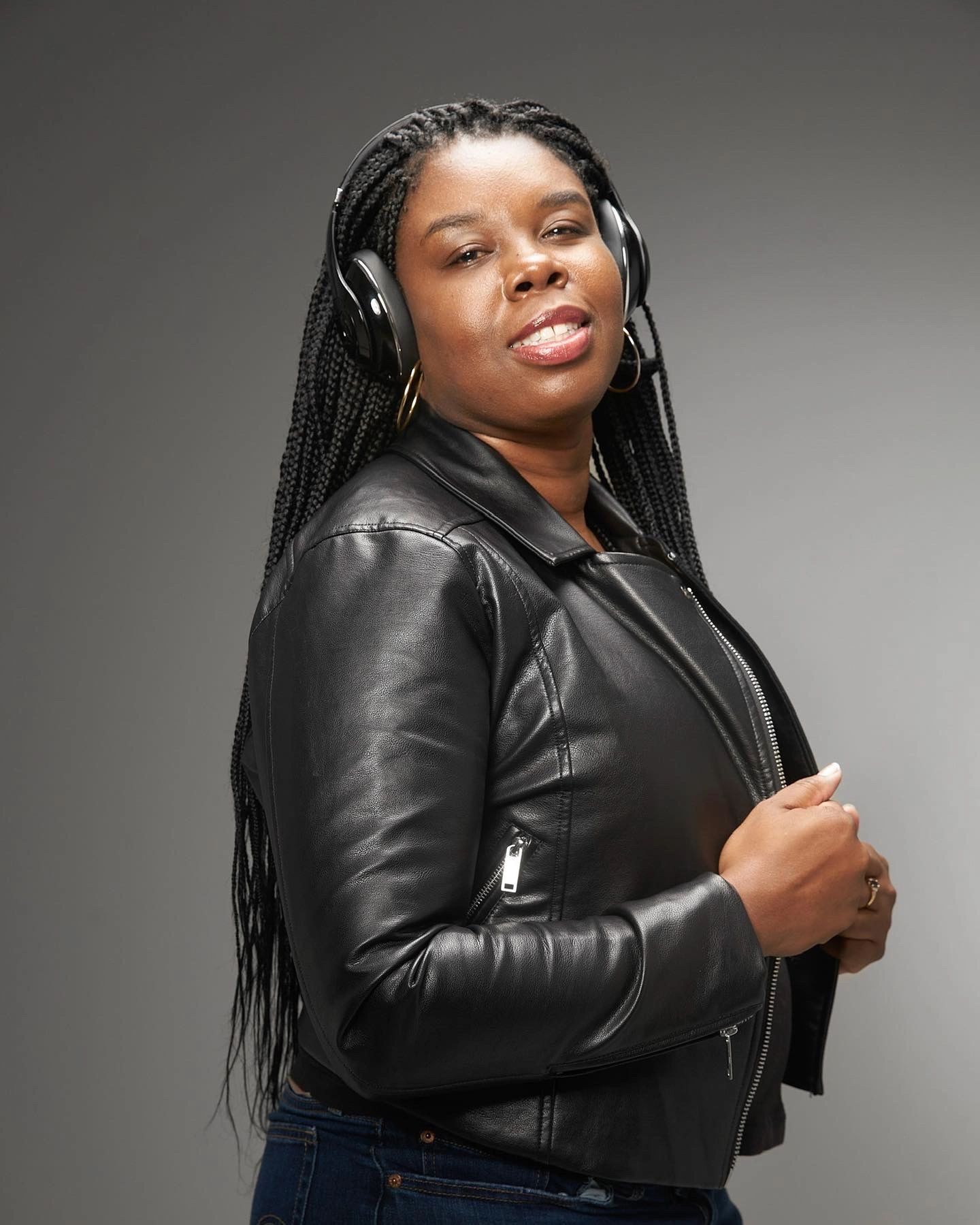 A Black woman in a leather jacket, long braids and headphones.