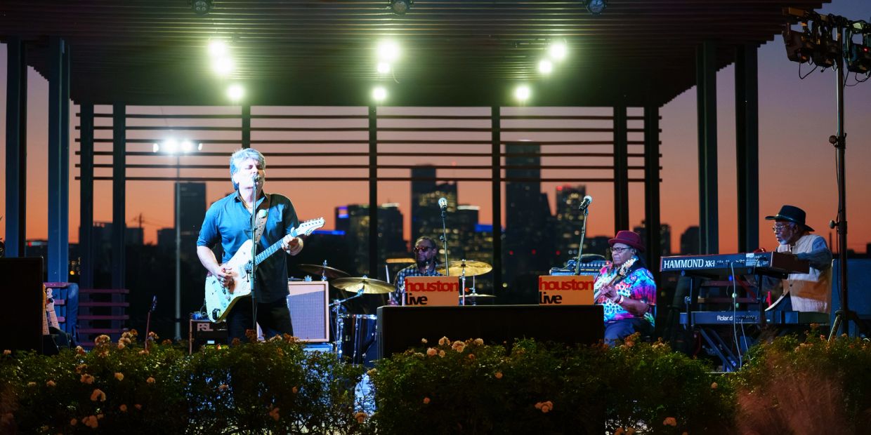 Band performing live at sunset with city skyline behind.