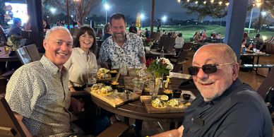 Four friends enjoying dinner together at an outdoor restaurant in the evening.