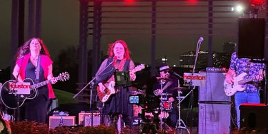 Band performing live on stage at night with city lights in the background.